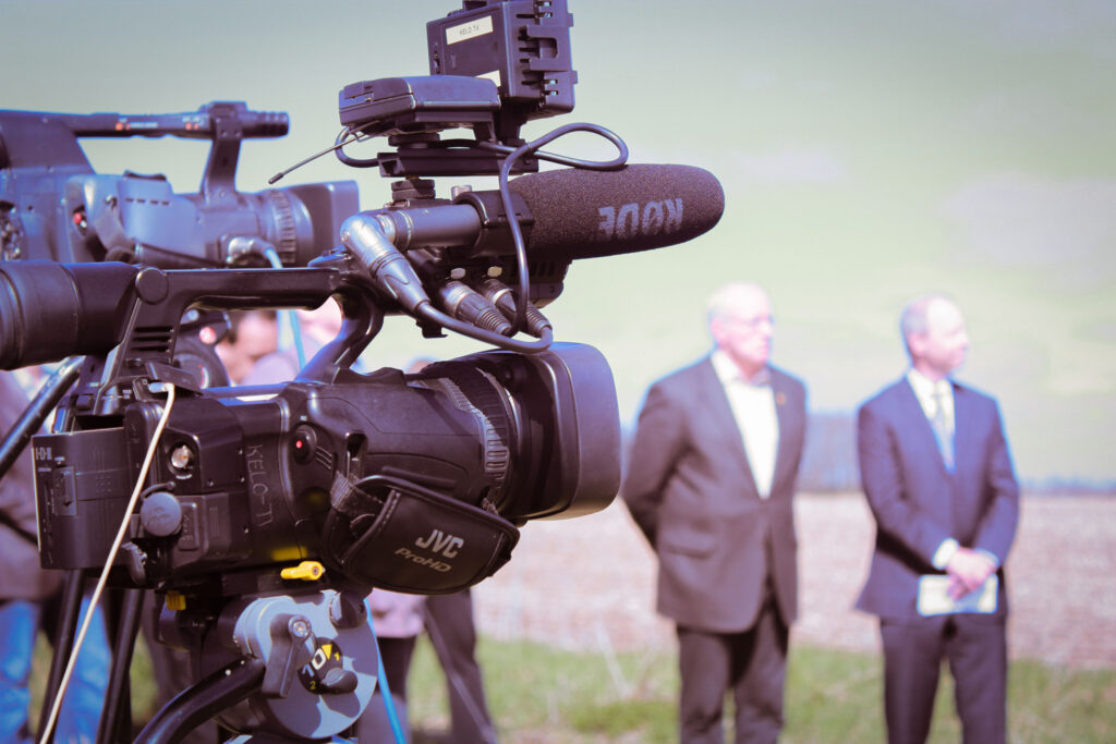 Cameras and people standing around at a press event.
