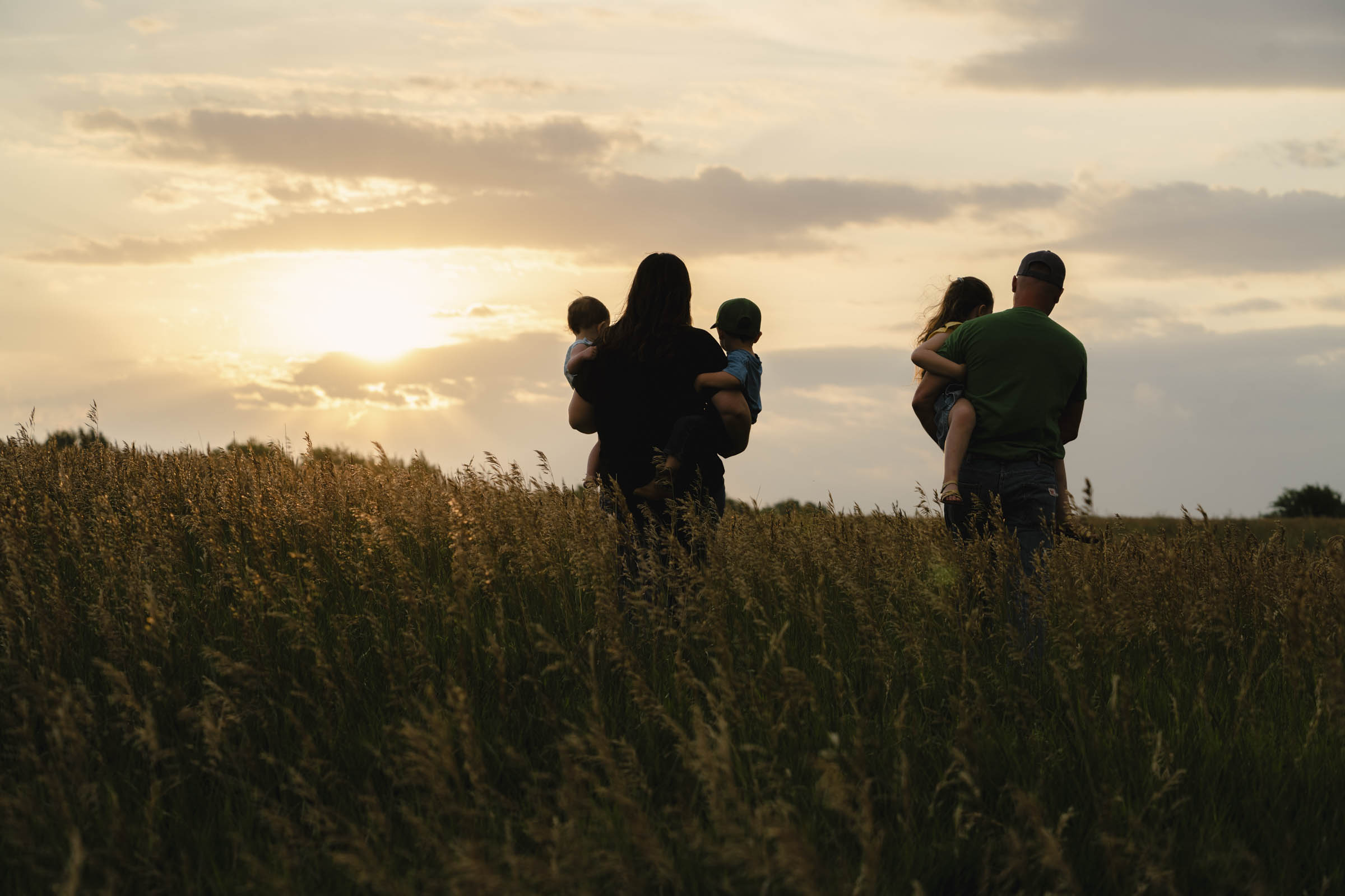 Woman and man walking towards sunset in a field, both are holding children.