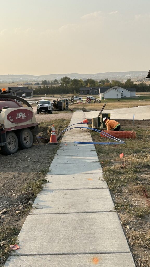 Broadband being installed near a sidewalk by a man in construction attire.