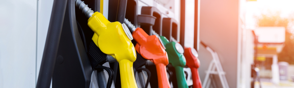 Gas pumps at a gas station in various colors with a sunset in the background.
