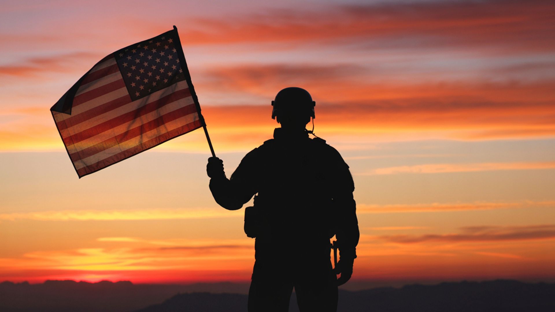 Silhouette of a soldier holding an American flag at sunset, representing national security and defense
