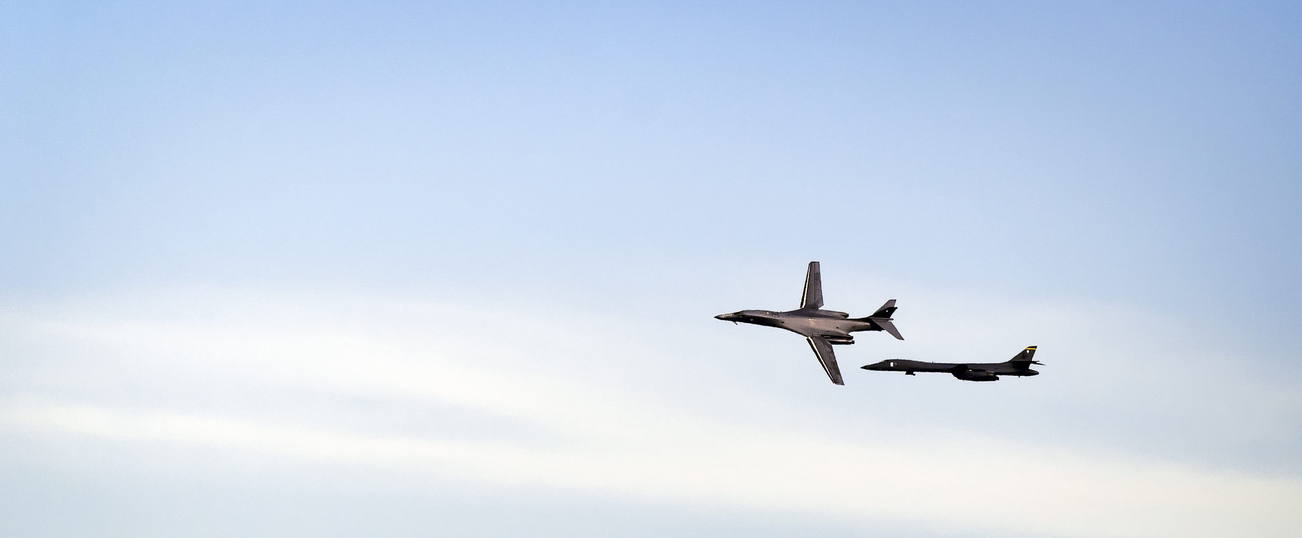 Two U.S. Air Force B-1B Lancer bombers flying in formation against a clear blue sky.