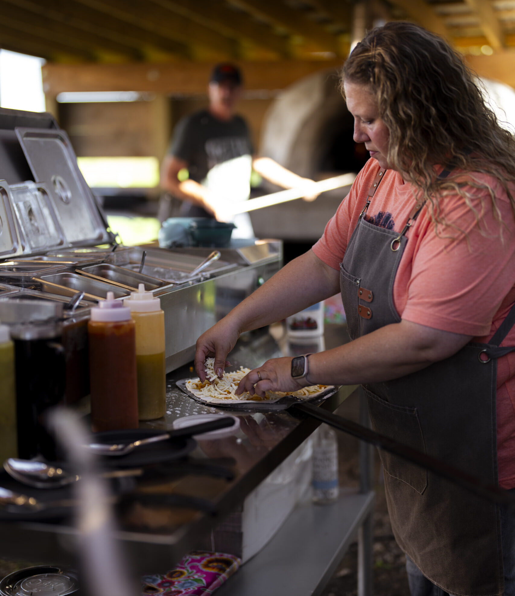 A woman prepares a pizza inside the kitchen area at Good Earth Farm near Lennox, South Dakota, with a wood-fired oven in the background.